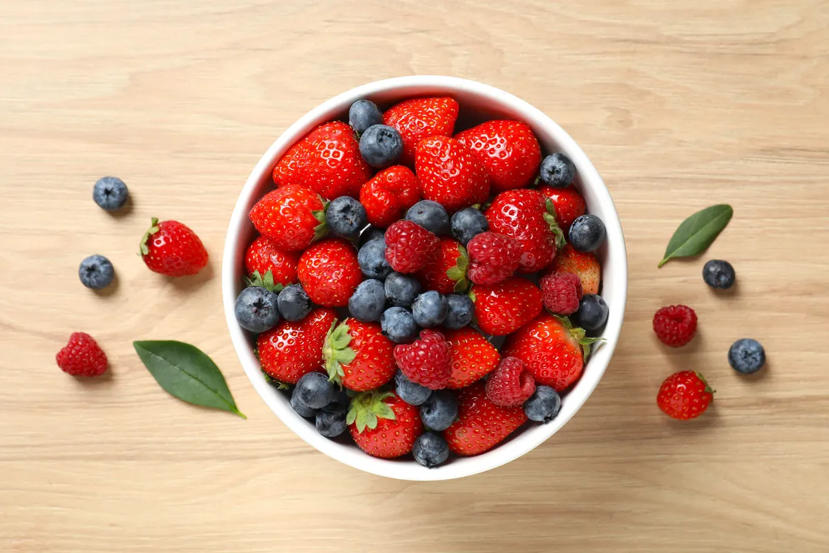 Different fresh ripe berries in bowl on wooden table, top view