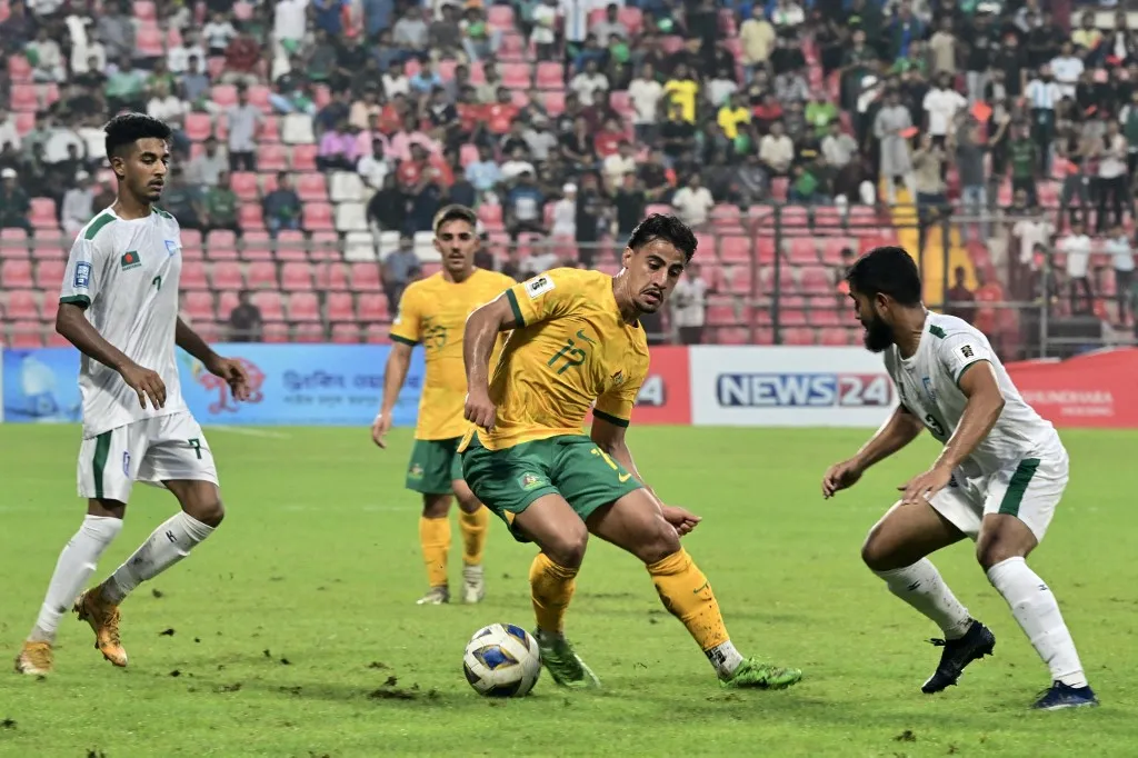 Fradi Australia's Daniel Arzani (C) fights for the ball with Bangladesh's Rahmat Mia (R) during the 2026 FIFA World Cup Asian qualification football match between Bangladesh and Australia at the Bashundhara Kings Arena in Dhaka on June 6, 2024. (Photo by MUNIR UZ ZAMAN / AFP)