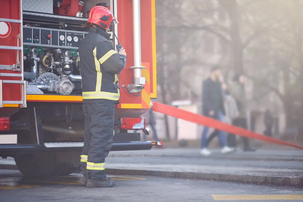 tűz, bozóttűz, Work of firefighters. Firefighter with uniform and helmet near a fire truck..