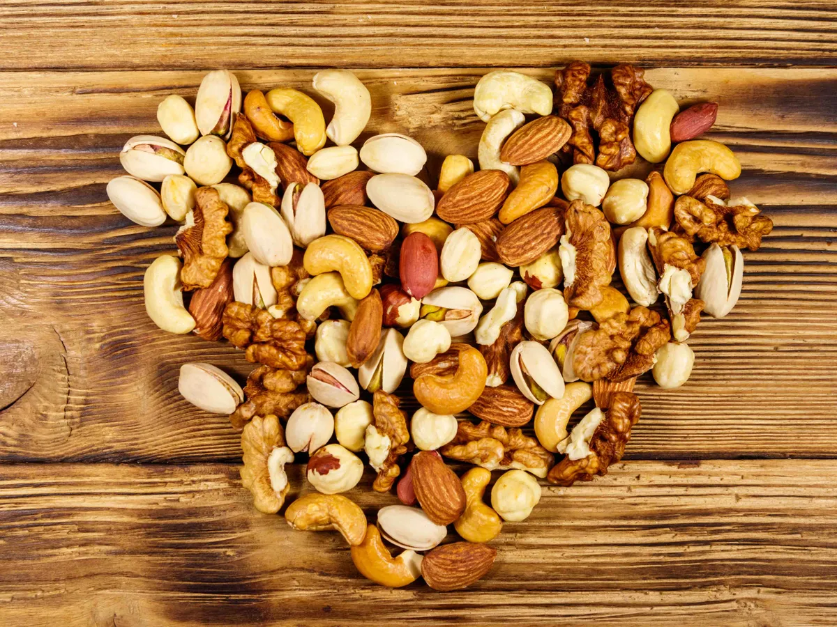 Pile of mixed nuts in shape of heart on wooden table. Top view. Walnuts, pistachio, almond, peanut, cashew, hazelnut on wood background. Healthy eating concept