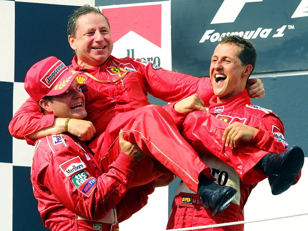 German Ferrari driver Michael Schumacher (R) and his teammate Brazilian Rubens Barrichello (L) hold their team Manager French Jean Todt on the podium of the Hungaroring racetrack near Budapest, 19 August 200, at the end of the Hungarian Formula One Grand Prix. With this victory Michael Schumacher gets his 4th World Champion crown and Ferrari wins the constructors' title.  AFP PHOTO PATRICK HERTZOG (Photo by Patrick HERTZOG / AFP)
