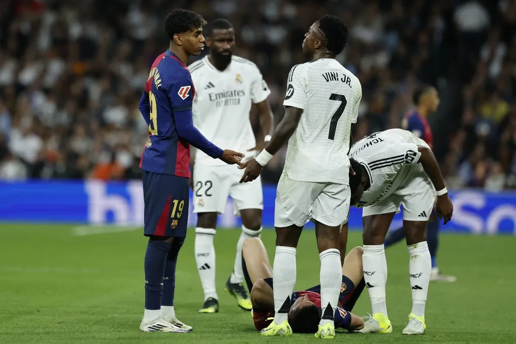 Barcelona's Spanish forward #19 Lamine Yamal (L) talks with Real Madrid's Brazilian forward #07 Vinicius Junior as Barcelona's Polish forward #09 Robert Lewandowski lies on the field during the Spanish league football match between Real Madrid CF and FC Barcelona at the Santiago Bernabeu stadium in Madrid on October 26, 2024. (Photo by OSCAR DEL POZO / AFP)