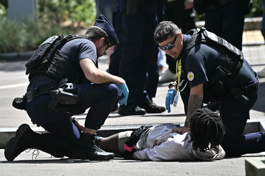 French Republican Security Corps (CRS - Compagnies Republicaines de Securite) officers  detain an injured individual suspected to have stabbed a police officer near the finish line area of the 4th stage of the 112th edition of the Tour de France cycling race, 174.2 km between Amiens Metropole and Rouen, Northern France, on July 8, 2025. Police opened fire on an individual, wounding him in the leg before detaining him after he attacked and injured a police officer with a knife, near the finish line area in Rouen before the arrival of the 4th stage of the Tour de France cycling race. (Photo by Loic VENANCE / AFP)