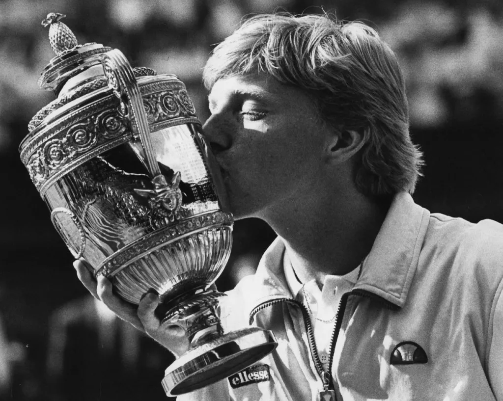 Picture taken 07 July 1985 shows German tennis star Boris Becker kissing the trophy after winning the Wimbledon Tennis Championships. Back in 1985 the flame-haired German turned the tennis world upside down when, at 17 years and 227 days he became the youngest player ever to win the All England Club crown, beating South African Kevin Curren. Becker was also the first unseeded player and the first German to win the men's event. Becker's Grand Slam career was ended on Wednesday 30 June 1999 when he was beaten 6-3, 6-2, 6-3 by Australian second seed Pat Rafter in the fourth round at Wimbledon.    (b/w only) (Photo by RUEDIGER SCHRADER / dpa Picture-Alliance via AFP)