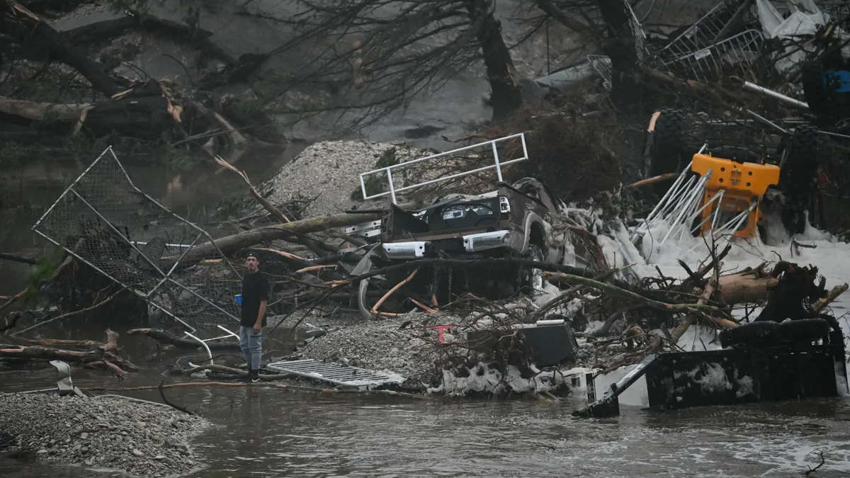 Texas, Egyesült Államok, árvíz,  Texasárvíz, A member of the public stands next to overturned vehicles and broken trees after flooding caused by a flash flood at the Guadalupe River in Kerrville, Texas, on July 5, 2025. Rescuers were desperately searching for at least 20 girls missing from a riverside summer camp, officials said on July 5, after torrential rains caused a "catastrophic" flash flood that killed at least 24 people as it swept through south-central Texas. (Photo by RONALDO SCHEMIDT / AFP)