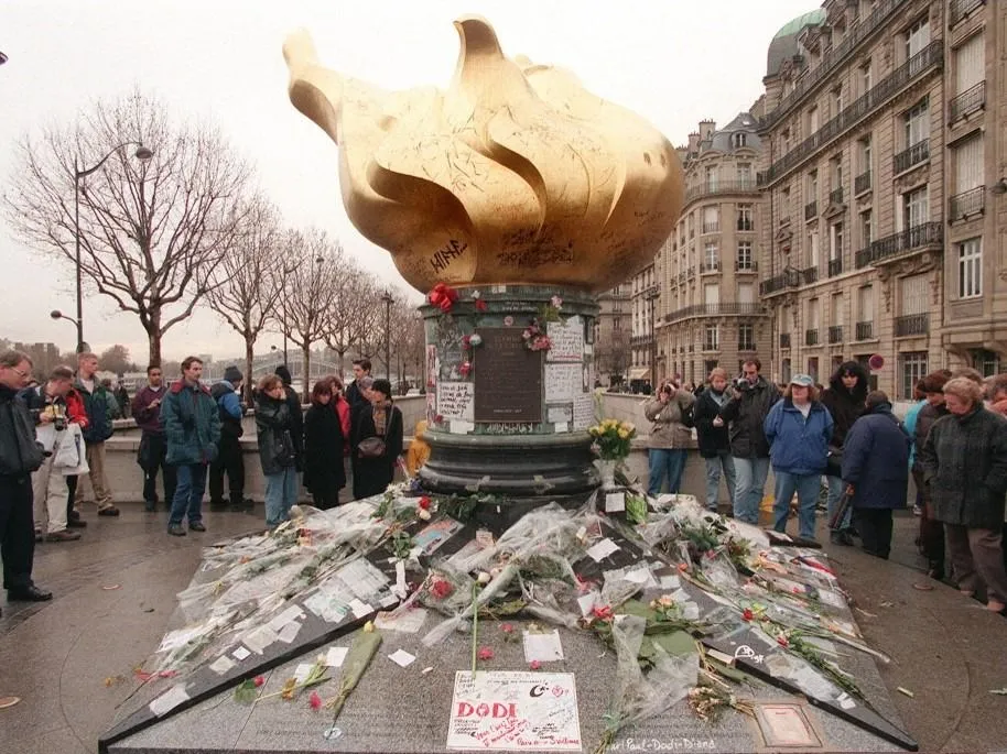 Des personnes se recueillent le 31 décembre près du pont de l'Alma à Paris, autour des gerbes déposées en mémoire de la Princesse Diana et de son ami égyptien, le milliardaire Dodi al-Fayed. Selon l'édition du 31 décembre du quotidien Aujourd'hui/Le Parisien, deux témoins affirment avoir aperçu une Fiat Uno blanche, conduite par un homme âgé d'eviron 40 ans, sortir du tunnel du pont de l'Alma en zigzagant, le 31 août dernier, relançant l'hypothèse de l'implication d'un véhicule dans l'accident ayant coûté la vie à la princesse Diana, son ami Dodi al-Fayed ainsi que le chauffeur. (Photo by JOEL SAGET / AFP)