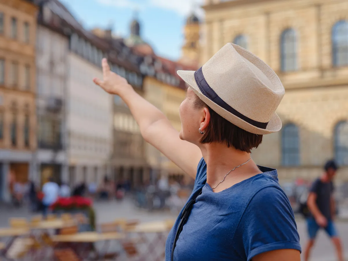 turizmus, summer female solo trip to Europe, happy young woman walking on european street, on the town building background in Munich. Having great vacation in Germany.