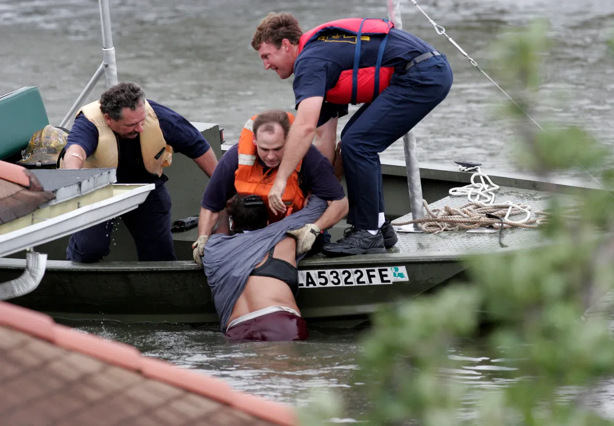 Rescue workers pull a woman from the water who was hanging onto the roof to escape the rising flood waters from Hurricane Katrina 29 August 2005 in New Orleans, Louisiana. Katrina was down graded to a category 4 storm as it approached New Orleans. (Chris Graythen/Getty Images/AFP) FOR NEWSPAPERS AND TV USE ONLY (Photo by Chris Graythen / Getty Images North America / Getty Images via AFP)