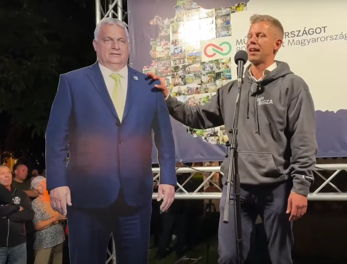 Magyar Péter bekattant, egy Orbán Viktor formájú papírbáb vállát veregeti. Forrás: YouTube