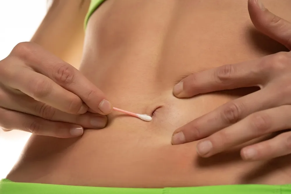 Woman cleaning her belly button with cotton swab , Cropped image, close up.