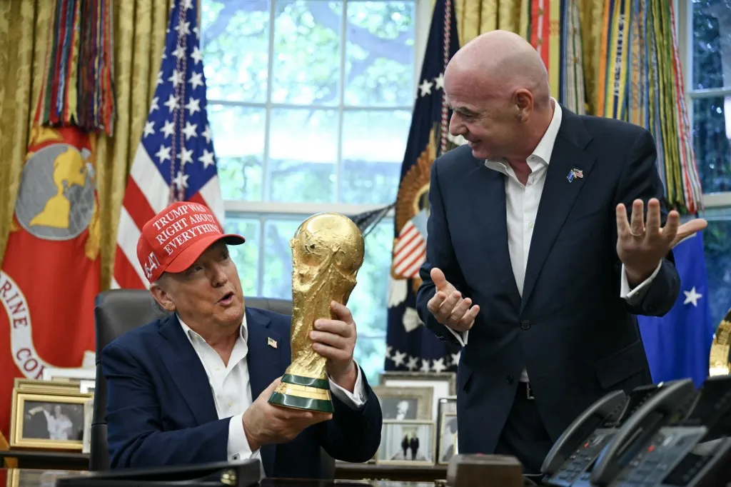 US President Donald Trump joined by FIFA president Gianni Infantino (R) holds the World Cup Trophy as he makes an announcement in the Oval Office of the White House in Washington, DC, on August 22, 2025. Trump announced the 2026 World Cup draw will be held on December 5 at Washington's Kennedy Center. (Photo by ANDREW CABALLERO-REYNOLDS / AFP)