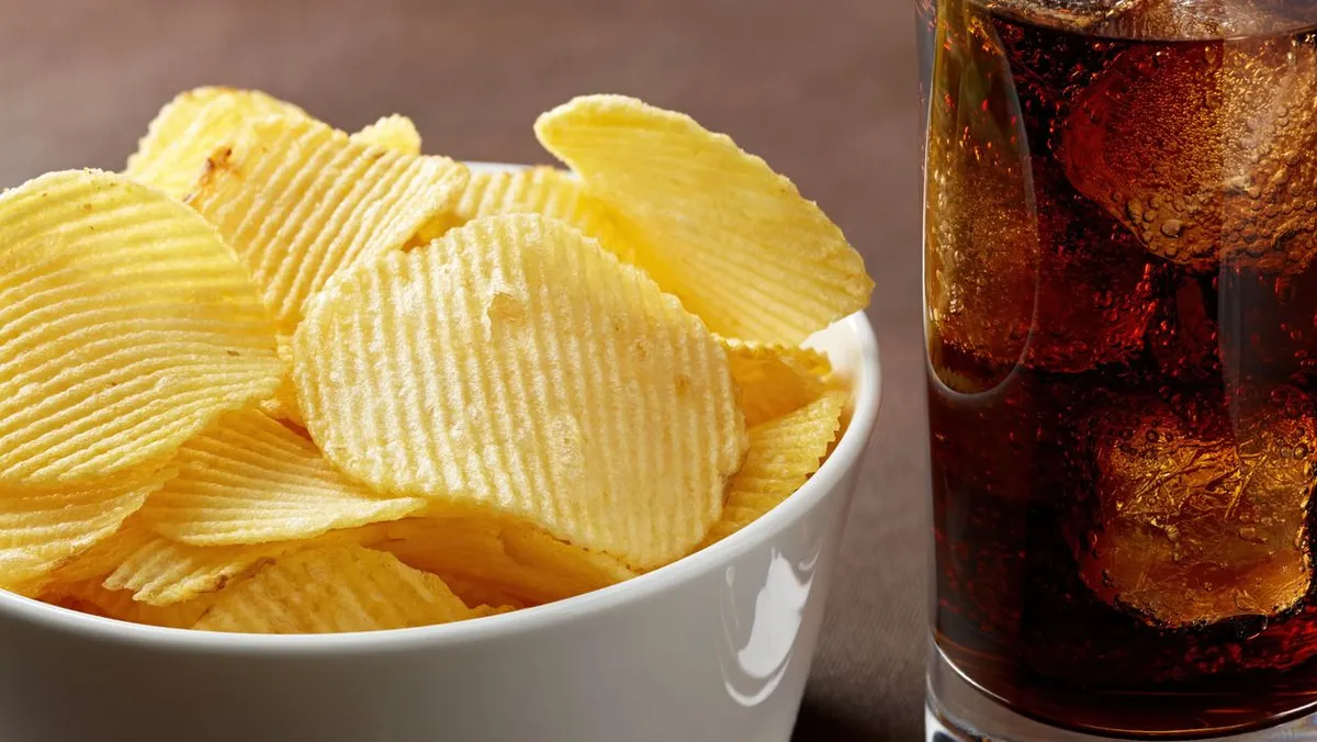 Potato chips in a white bowl and a glass of cola with ice. Close up macro view, feldolgozott ételek