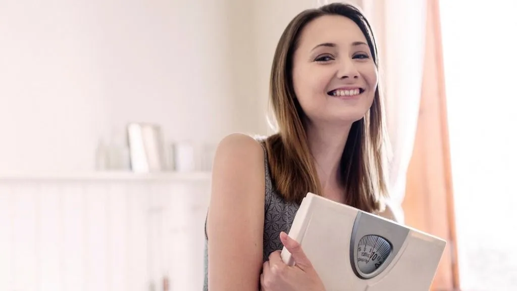 menorexia Woman holding bathroom scales looking at camera smiling (Photo by Innocenti / Connect Images via AFP)
