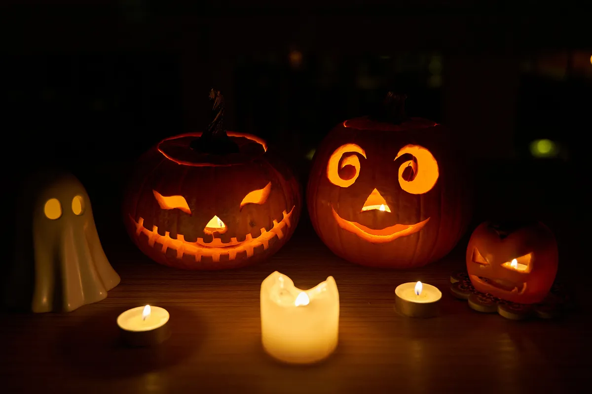 Spooky season halloween decor. Carved pumpkins by miniature ghost and child Jack-o'-lantern with candles