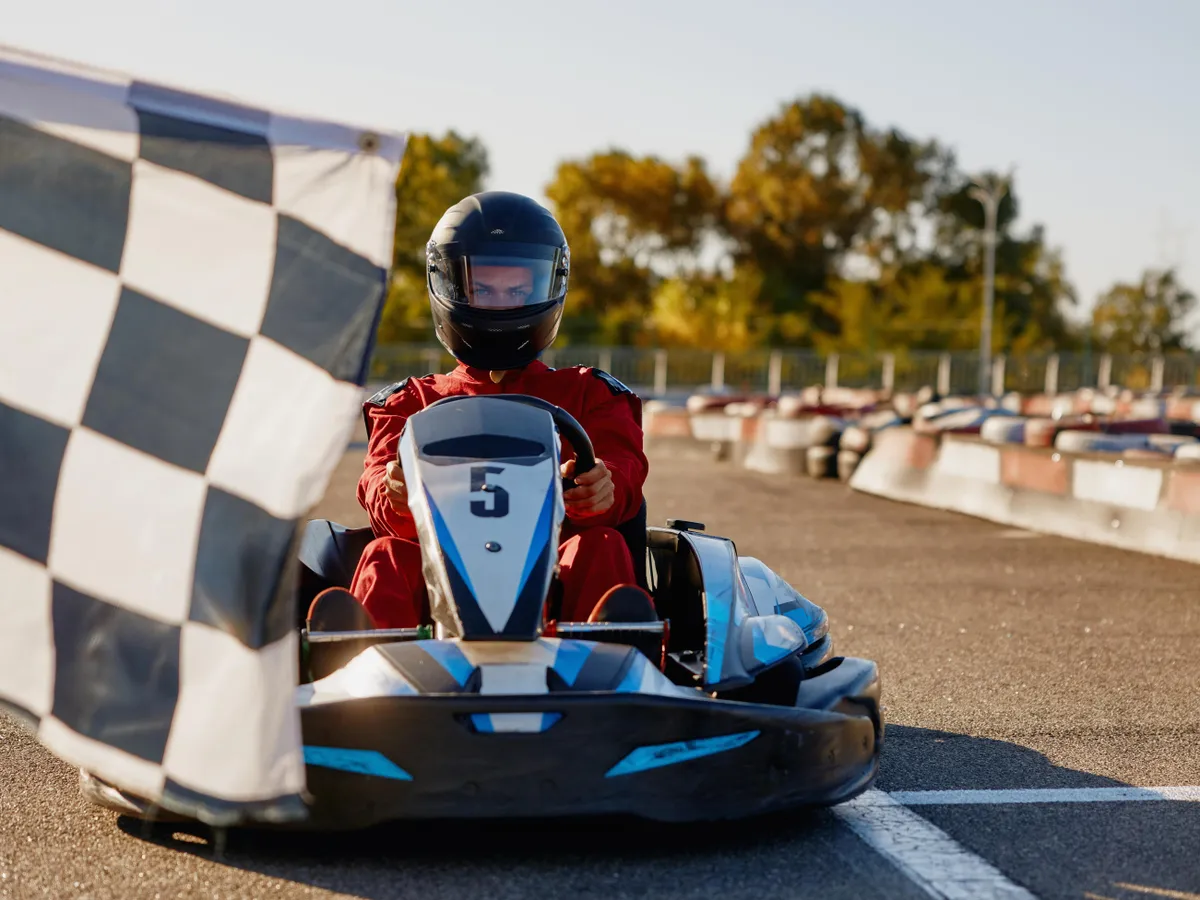 Go-kart driver crossing at finish line moving to checkered racing flag