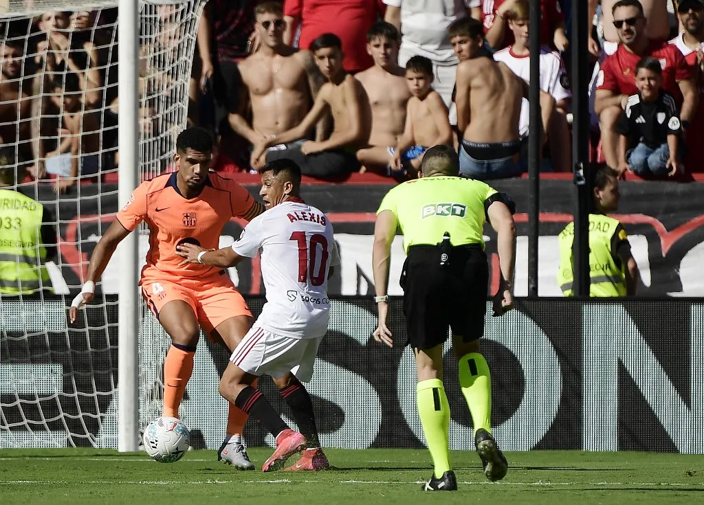 Barcelona's Uruguayan defender #04 Ronald Federico Araujo da Silva (L) and Sevilla's Chilean forward #10 Alexis Sanchez vie for the ball during the Spanish league football match between Sevilla FC and FC Barcelona at Ramon Sanchez Pizjuan Stadium in Seville on October 5, 2025. (Photo by CRISTINA QUICLER / AFP)