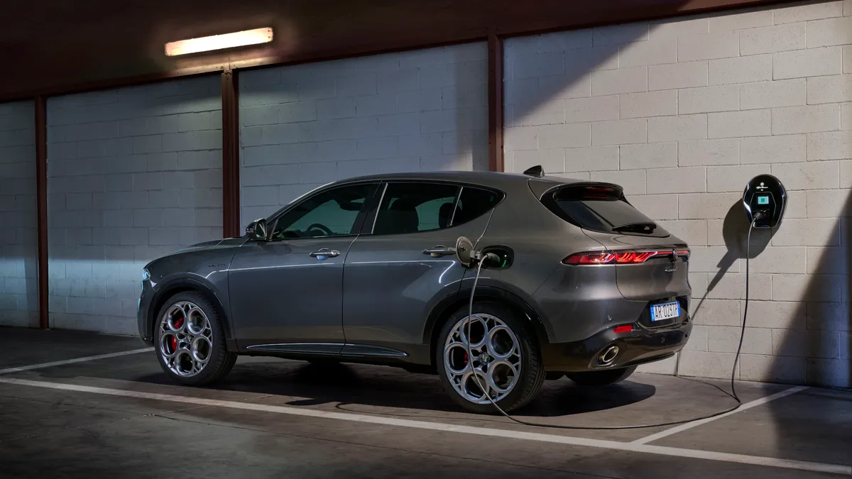 Egy Alfa Romeo Tonale plug-in hibrid parkol elektromos fali töltődobozhoz csatlakoztatva.