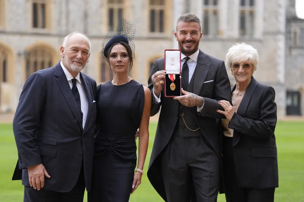 Former England footballer David Beckham (2R) poses next to his wife singer and fashion designer Victoria Beckham (L) and his parents Ted (L) and Sandra (R) with his medal after being appointed as a Knight Bachelor (Knighthood) for services to sport and charity at an investiture ceremony at Windsor Castle on November 4, 2025. (Photo by Andrew Matthews / POOL / AFP)