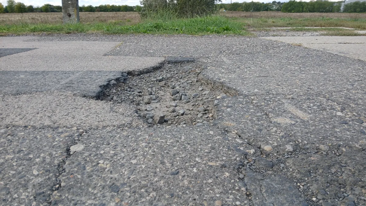 Egy éles peremű kátyú egy út közepén.