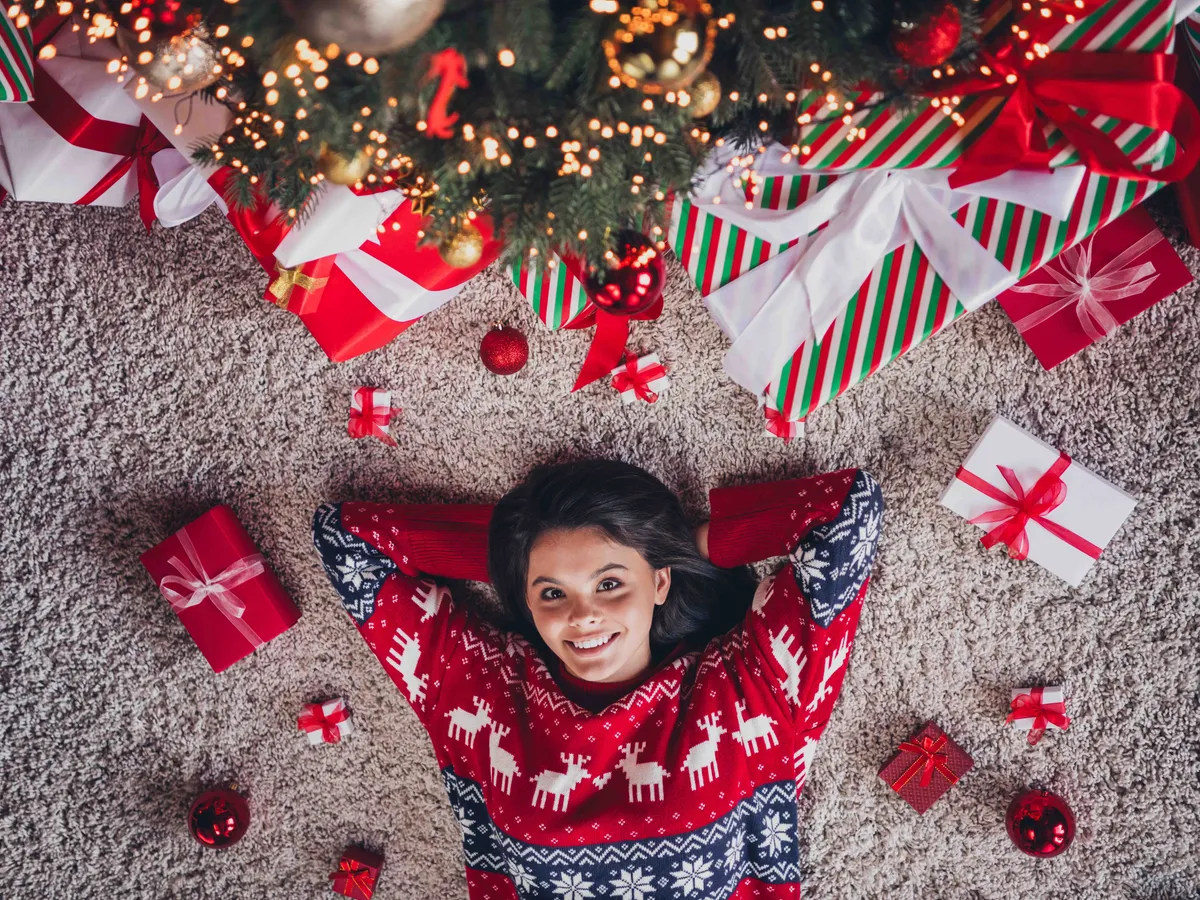 High view photo of pretty lovely girl dressed new red print clothes hands above head lying floor enjoying christmas decorations indoors