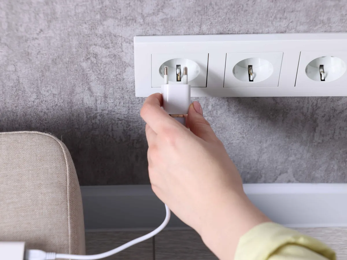 Woman plugging power bank into socket on grey wall indoors, closeup