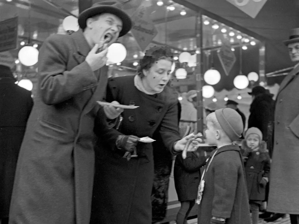 karácsonyivásár, karácsonyi vásár,
Parents and their little son in front of a snack bar booth at the christmas market eating sausages, Germany 1930s. (Photo by Heinz Pollmann / United Archives/Pollmann / mauritius images via AFP)
