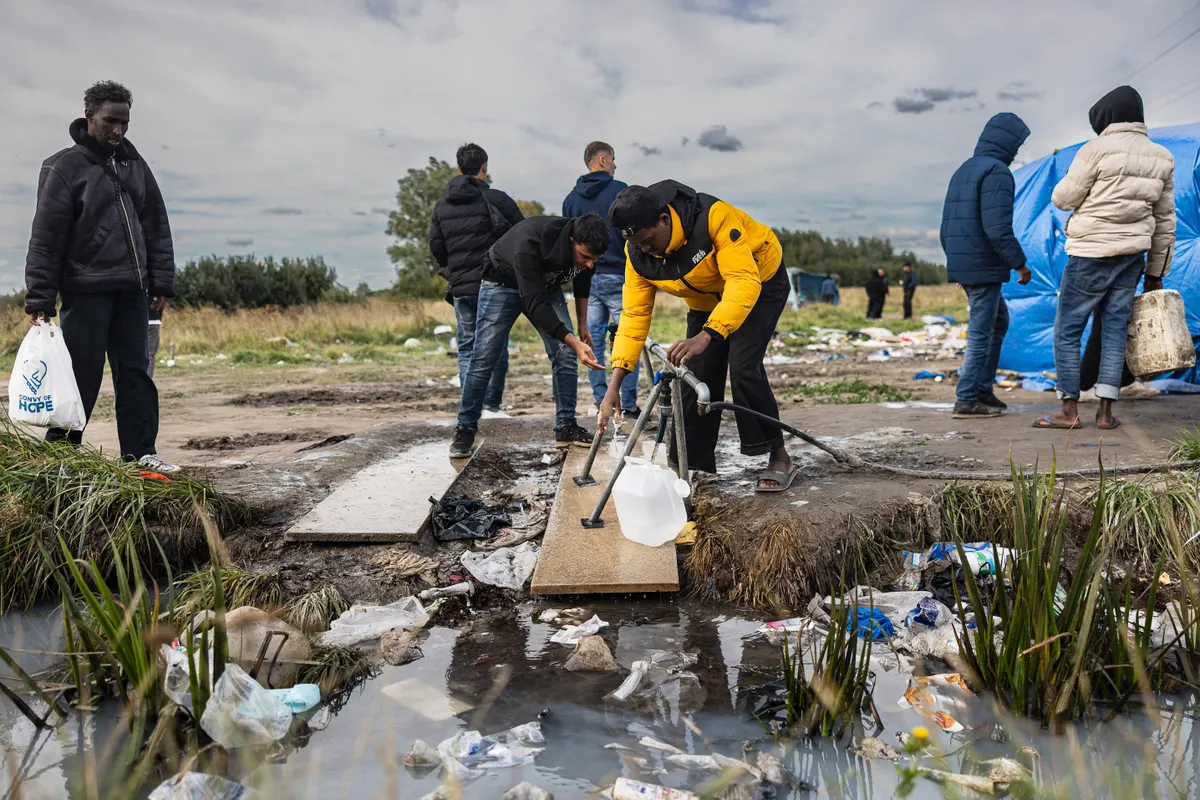 Migrant fills water containers at a migrants' makeshift camp in Loon-Plage, near Dunkirk, northern France on September 24, 2025. (Photo by Sameer Al-DOUMY / AFP)