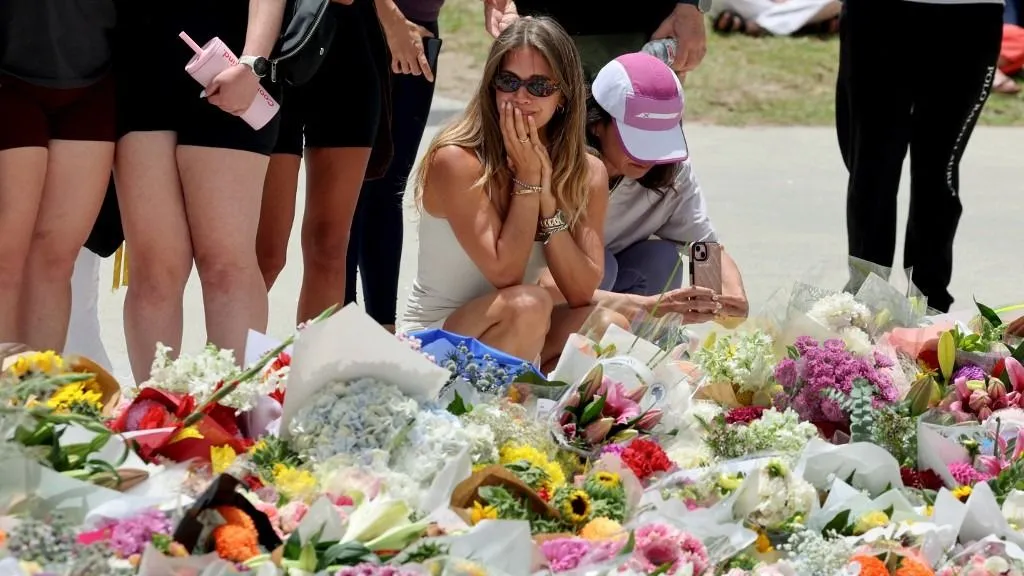 ausztráliai terrortámadás, Mourners gather by floral tributes at the Bondi Pavillion in memory of the victims of a shooting at Bondi Beach, in Sydney on December 15, 2025. A father-and-son team toting long-barrelled guns shot and killed 15 people including a 10-year-old girl at Sydney's Bondi Beach on December 14, with authorities labelling it an antisemitic terrorist attack on a Jewish festival. (Photo by DAVID GRAY / AFP)
