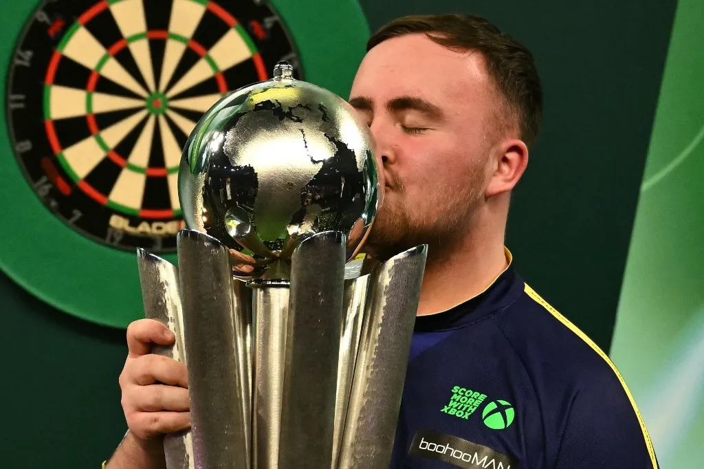 England's Luke Littler kisses the Sid Waddell Trophy after victory over Netherlands' Michael van Gerwen in the PDC World Darts Championship final, at Alexandra Palace in London on January 3, 2025. Luke Littler became darts' youngest world champion at just 17 after thrashing three-time winner Michael van Gerwen in front of an adoring home crowd at London's Alexandra Palace on Friday. This time there was no stopping "Luke the Nuke" as he stormed past Dutchman Van Gerwen by seven sets to three. (Photo by Ben STANSALL / AFP)