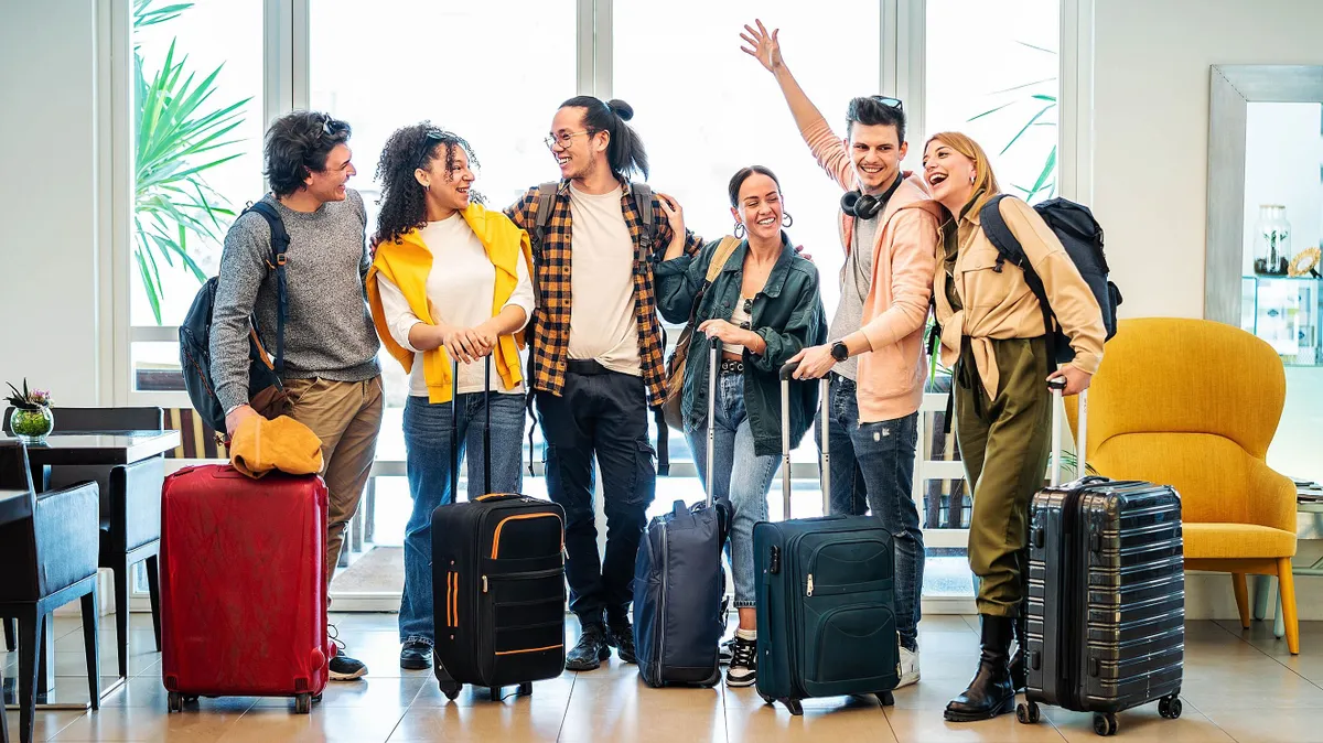 hazai turizmus, Young group of tourists with suitcases arriving at youth hostel guest house - Happy friends enjoying summer vacation together - Millenial people doing check-in at hotel lobby - Summertime holidays