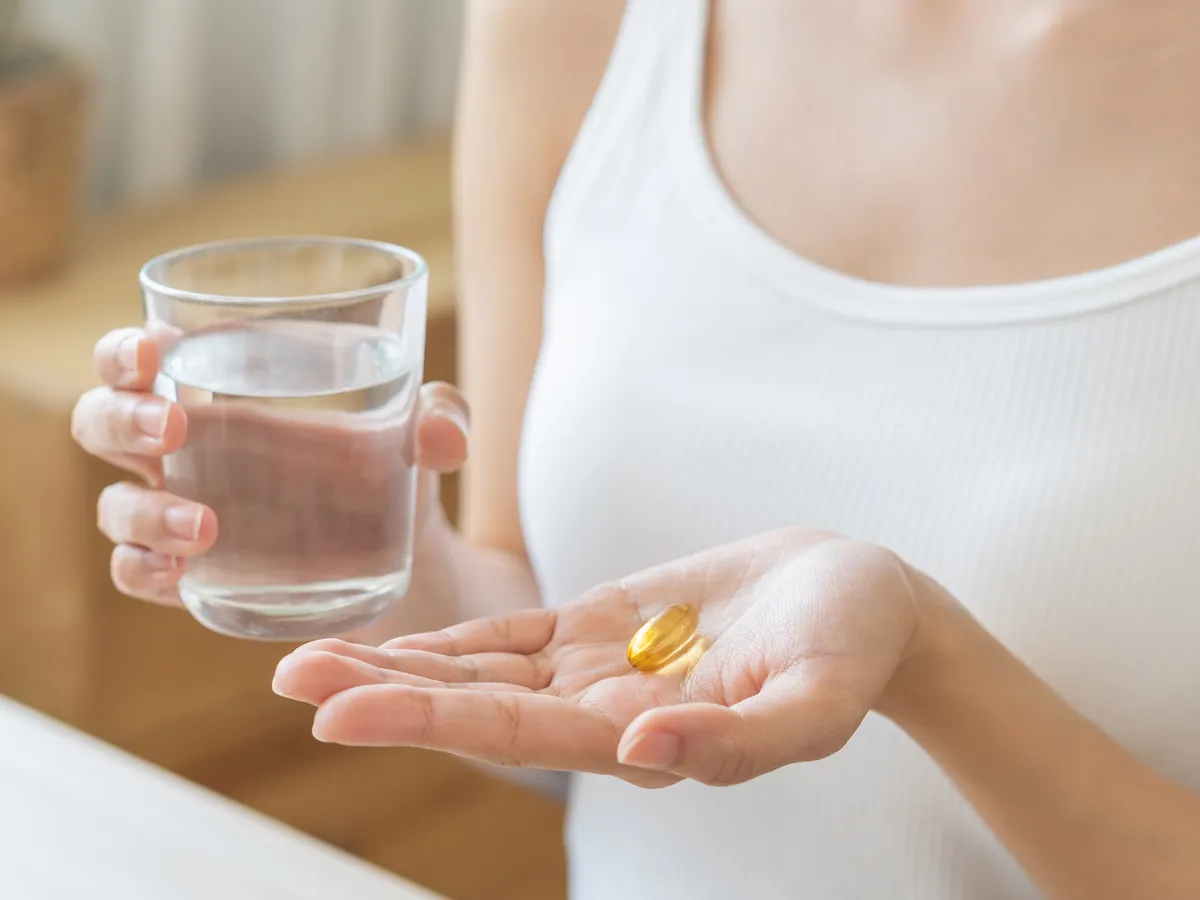 Dietary supplement, asian young woman, girl hand holding medical pill capsule, take or eat vitamin C, D for treatment for skin, hair and nail strengthen with glass of pure water at home, healthcare.