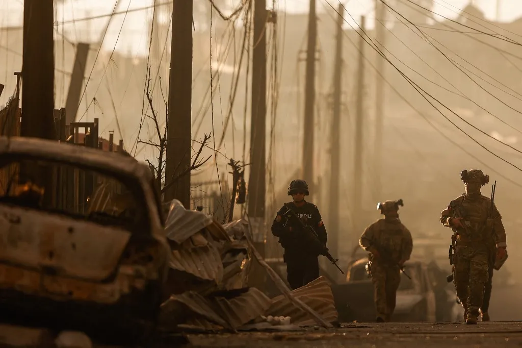 Chilean soldiers patrol among the damage after a wildfire in Concepcion, Chile on January 18, 2026. Uncontrolled wildfires tore through communities in southern Chile, leaving charred ruins in their wake and at least 19 dead, authorities said on January 18, 2026. (Photo by Raul BRAVO / AFP)