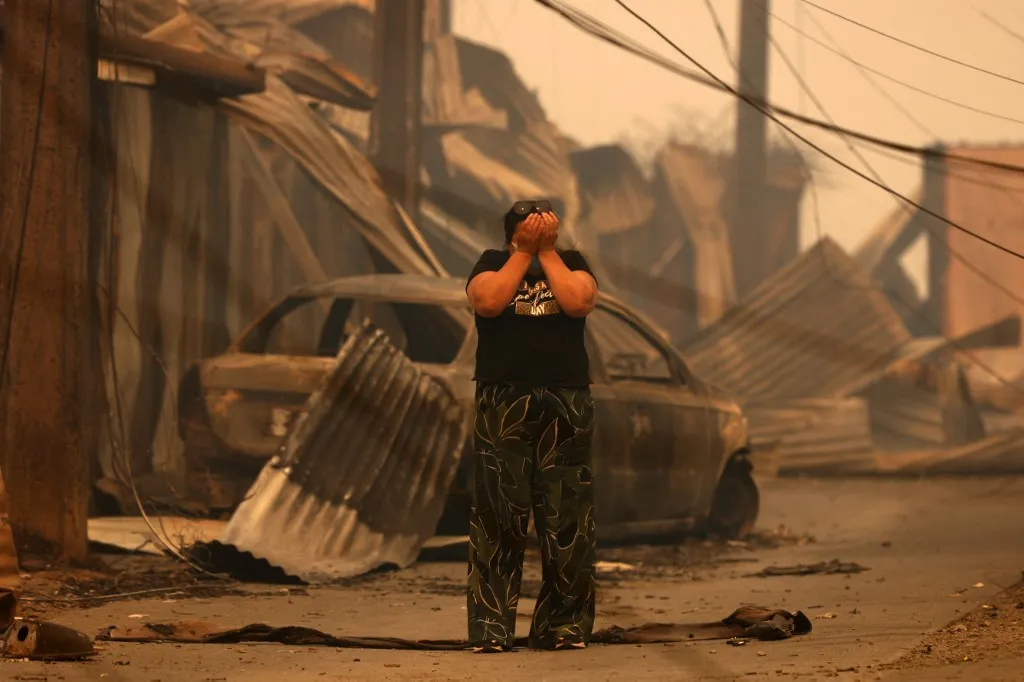 természeti katasztrófa és erdőtüzek Chilében, A resident reacts in front of the charred remains of destroyed homes and a vehicle after a wildfire in Concepcion, Chile, on January 18, 2026. Wildfires raging in southern Chile have killed at least 15 people and forced more than 50,000 to evacuate, the government said. (Photo by Raul BRAVO / AFP)