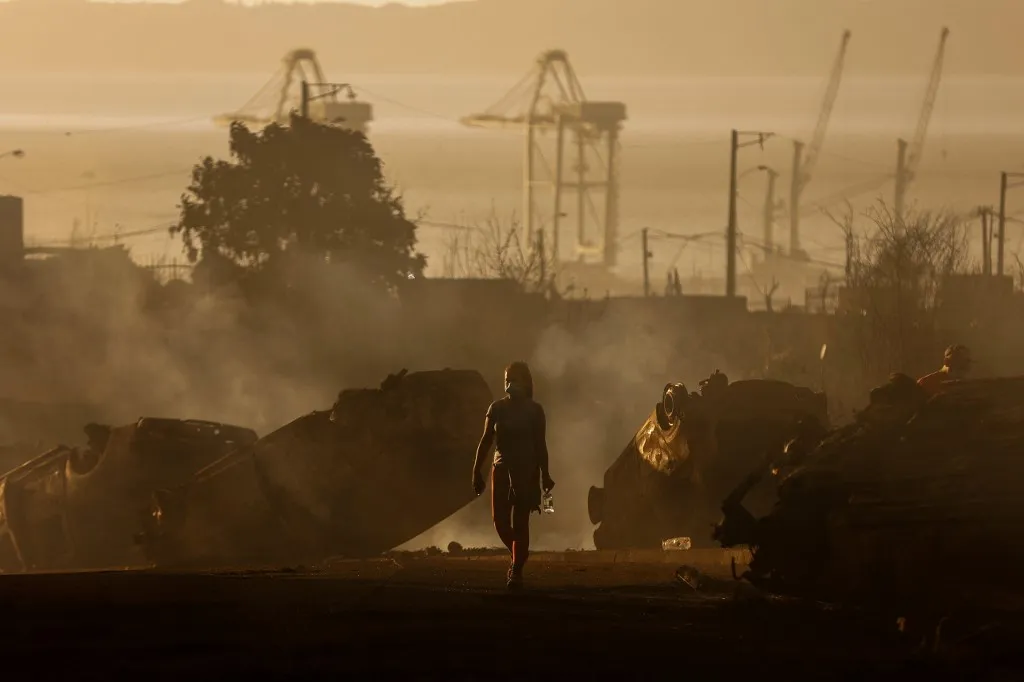 A woman walks among burned-out cars after a wildfire in Concepcion, Chile on January 18, 2026. Uncontrolled wildfires tore through communities in southern Chile, leaving charred ruins in their wake and at least 19 dead, authorities said on January 18, 2026. (Photo by Raul BRAVO / AFP)