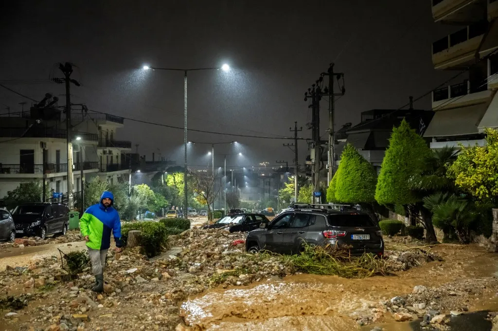 People triy to clean a flooded street covered with rubbles after a heavy rainfalls in Ano Glyfada, southern of Athens, on January 21, 2026. (Photo by Aris MESSINIS / AFP)