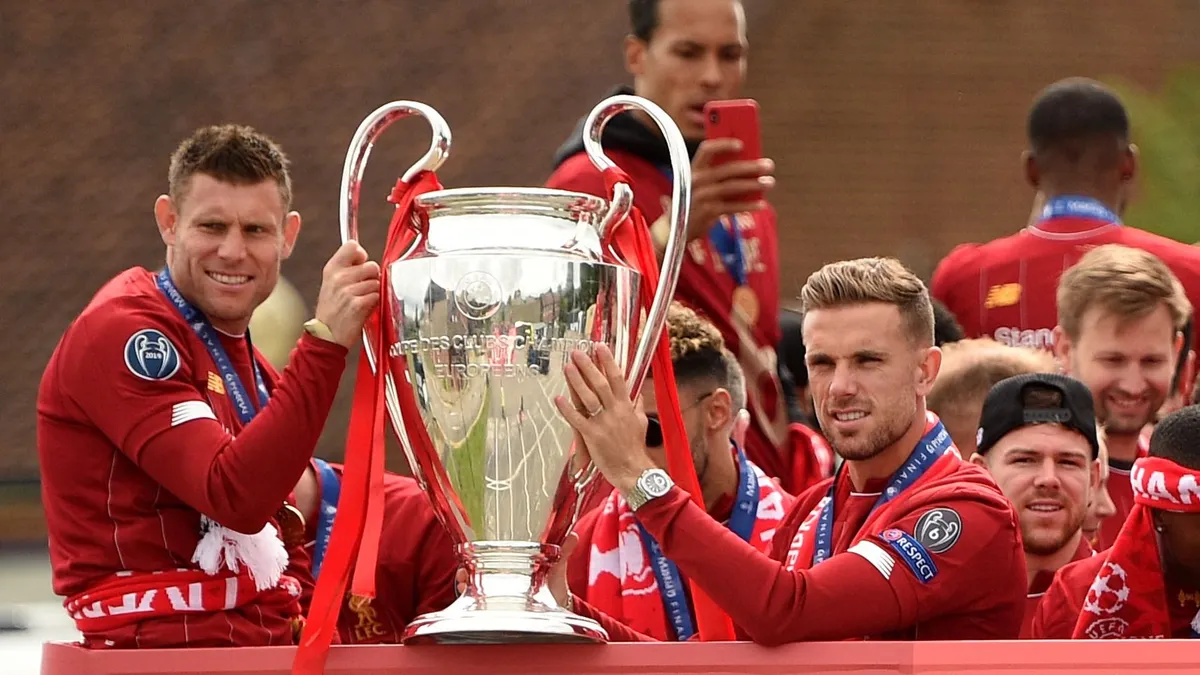 Liverpool's English midfielder James Milner (L) and Liverpool's English midfielder Jordan Henderson hold the European Champion Clubs' Cup trophy during an open-top bus parade around Liverpool, north-west England on June 2, 2019, after winning the UEFA Champions League final football match between Liverpool and Tottenham. Liverpool's celebrations stretched long into the night after they became six-time European champions with goals from Mohamed Salah and Divock Origi to beat Tottenham -- and the party was set to move to England on Sunday where tens of thousands of fans awaited the team's return. The 2-0 win in the sweltering Metropolitano Stadium delivered a first trophy in seven years for Liverpool, and -- finally -- a first win in seven finals for coach Jurgen Klopp. (Photo by Oli SCARFF / AFP)