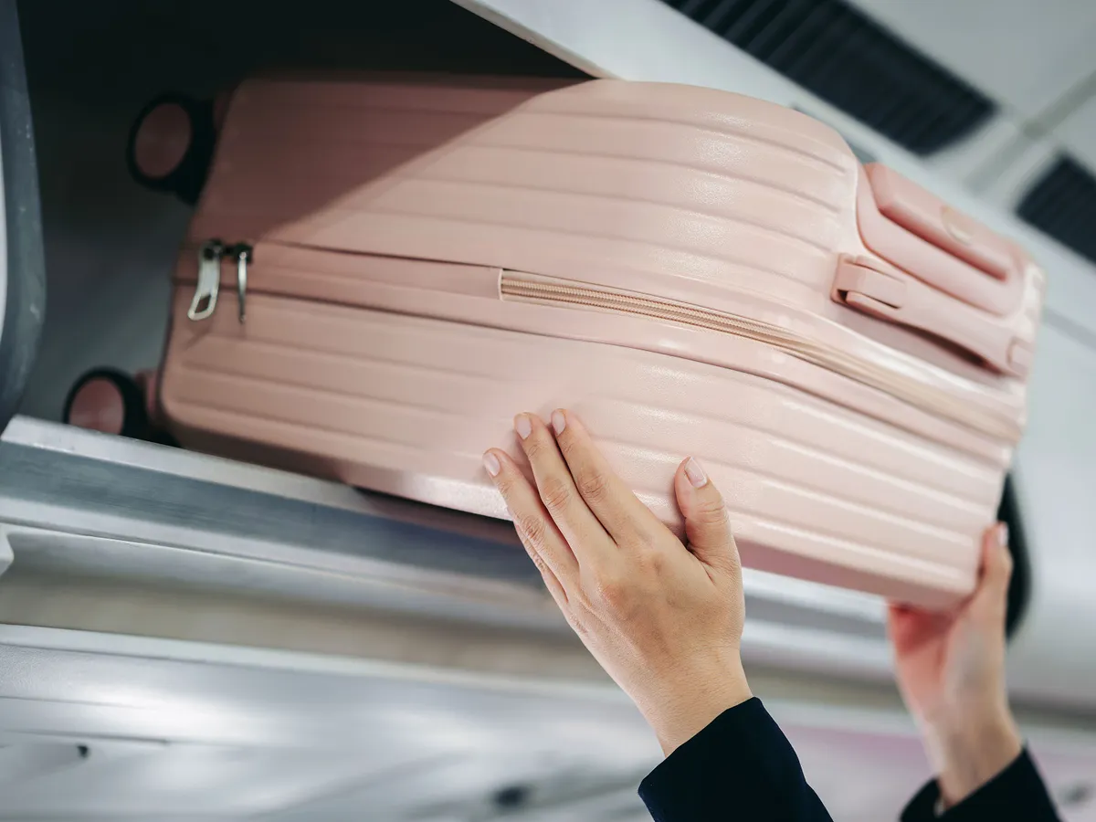Close up view hands placing travel bag in overhead airplane storage preparing for international flight trip journey