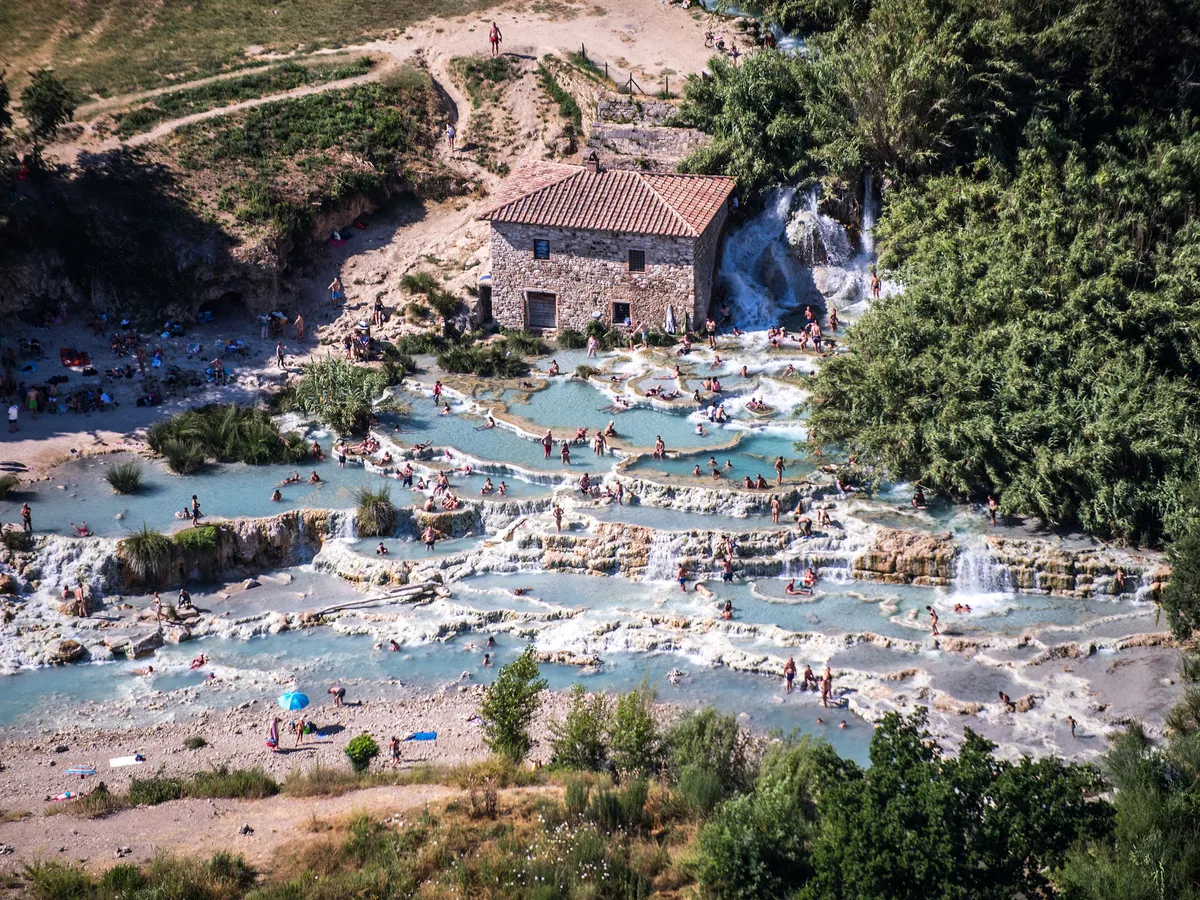 GROSSETO, ITALY - JULY 01: Aerial view, from a helicopter, of tourists at the Terme di Saturnia, Italy's most famous thermal spring, located in Tuscany a few kilometres from Grosseto, its sulphurous waters flow from underground at a rate of 800 litres per second and a constant temperature of 37° Centigrade on July 01, 2019 in Grosseto, Italy. Italy's nearly 8000 km (5,000 miles) coastlines and islands stretch across the Mediterranean Sea and attract large numbers of both local and foreign tourists during the summer season. (Photo by Fabrizio Villa/Getty Images)