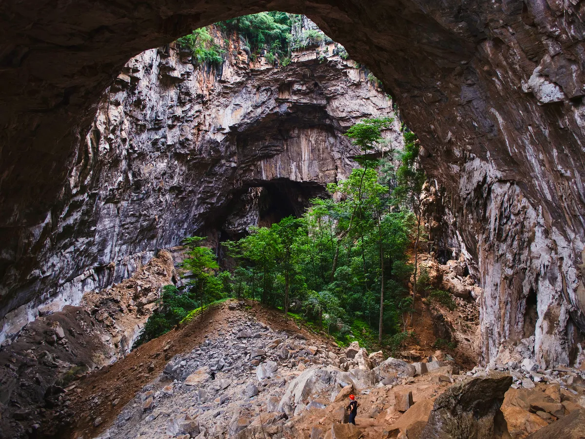 A visitor stands at the entrance of a cave in the Peruaçu Caves National Park, home to a group of more than 250 caves with rock paintings dating back approximately 12,000 years, in the municipality of Itacarambi, Minas Gerais State, Brazil, on January 9, 2025. The United Nations Educational, Scientific and Cultural Organization (UNESCO) declared the Peruacu Caves National Park a World Natural Heritage Site on July 13, 2025 during a session of the World Heritage Committee in Paris. (Photo by Evandro Pereira / AFP)
