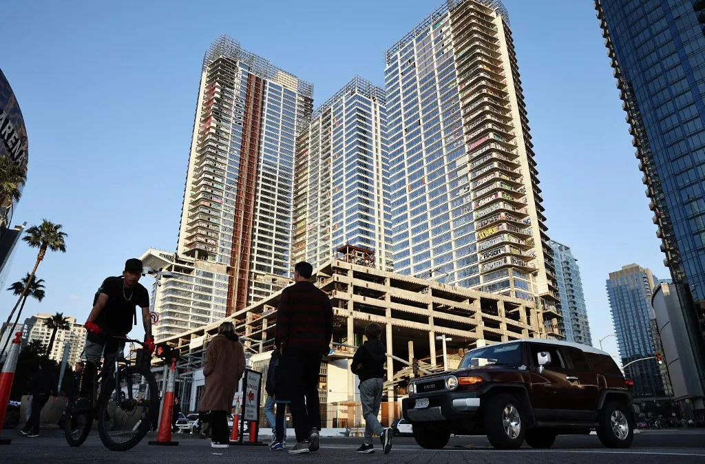 LOS ANGELES, CALIFORNIA - MARCH 20: People pass beneath the so-called Graffiti Towers, where graffiti writers tagged 40 floors of an unfinished luxury skyscraper development last month, on March 20, 2024 in Los Angeles, California. Construction of the $1 billion Oceanwide Plaza luxury real estate development stalled in 2019 after a China-based developer ran out of funding leaving the three-tower project unfinished amid a housing crisis in the city. The project is located across the street from the Crypto.com Arena and its value has plummeted since its appraisal in 2017, according to the projects creditors. Some view the tagging as a work of graffiti art while city officials will pay nearly $4 million to secure the site and clean the graffiti. Mario Tama/Getty Images/AFP (Photo by MARIO TAMA / GETTY IMAGES NORTH AMERICA / Getty Images via AFP)