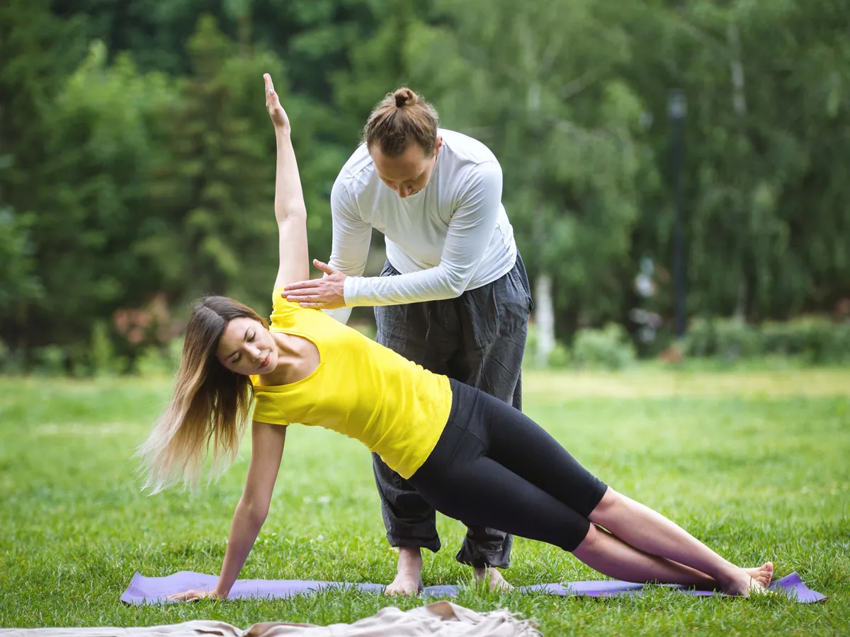 Yoga in morning park - instructor is training young women for flexibility, telephoto