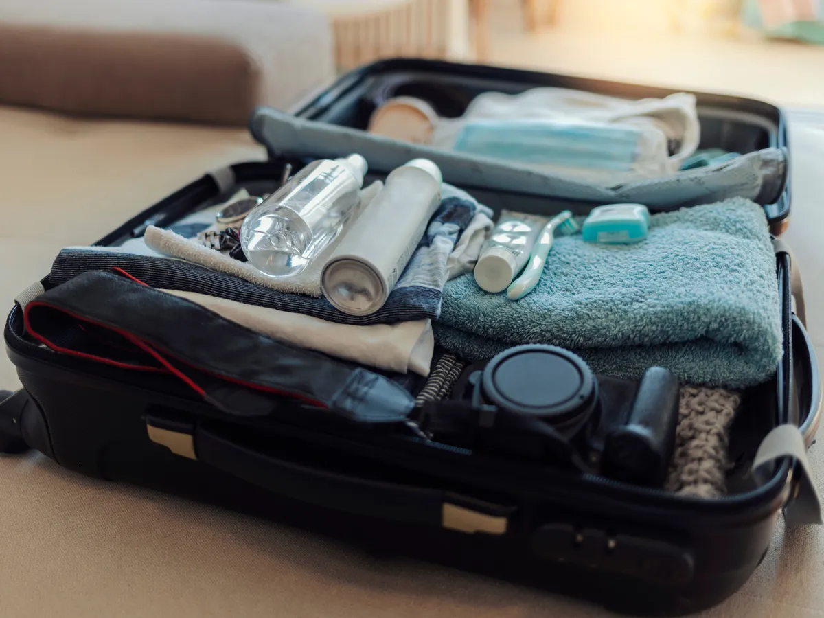 Travel passports and medical masks are on the travel suitcase. Protective face mask packed into a suitcase along with clothes and a camera, COVID-19 prevention concept. Healthcare and medical concept.