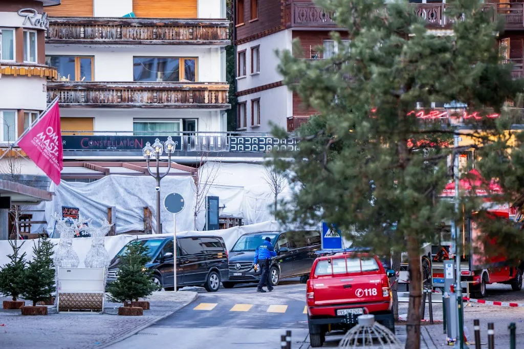 A svájci tűzeset helyszíne 2026. január 1-jén Funeral service vehicles arrive near the bar Le Constellation where a fire ripped through the venue during New Year's Eve celebrations in Crans-Montana, on January 1, 2026. Several dozen people are presumed dead and around 100 injured after a fire ripped through a crowded bar in the luxury Swiss ski resort of Crans-Montana, Swiss police said on January 1, 2026. Police, firefighters and rescuers rushed to the popular resort, which is set to host the Ski World Cup from January 30, after the fire broke out in the early hours of New Year's Day. (Photo by MAXIME SCHMID / AFP)