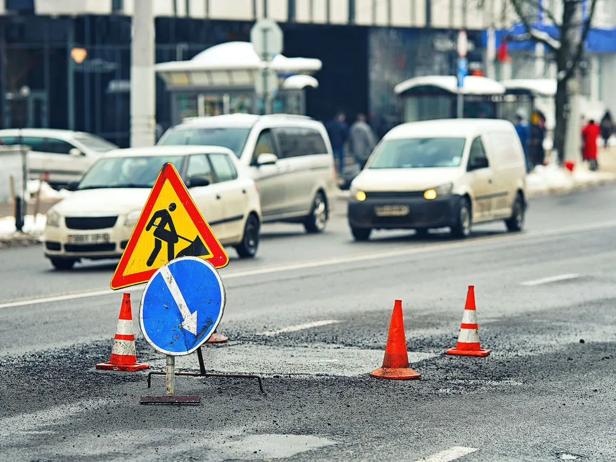Asphalt pavement patching, pothole repair work. Patching potholes, resurfacing roadway. Road construction warning zone with visible traffic signs and cones, repair work process. Asphalt patchwork