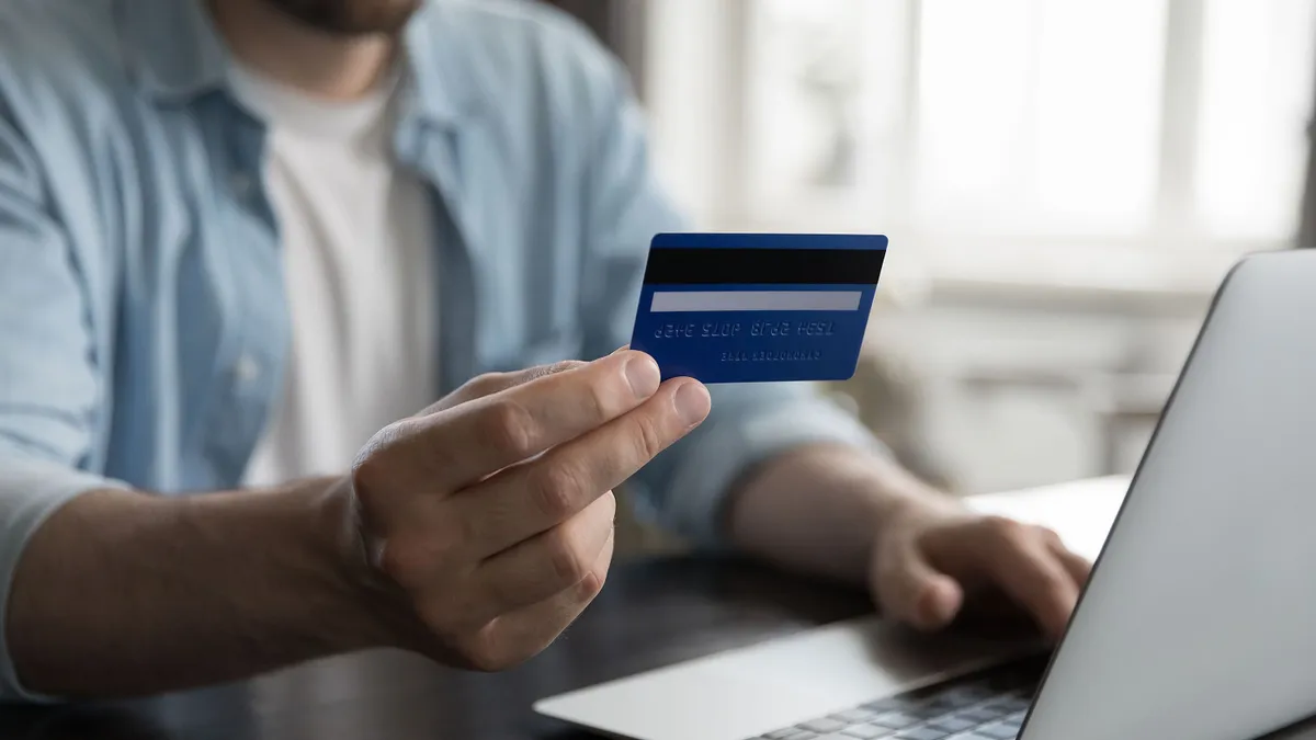 Close up view male hand holding credit card using laptop make on-line payments via e-bank application, do remote e-shopping at home. Secure e-payment, e-commerce client, instant money transfer concept