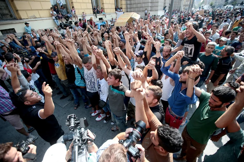 Syrian and Afgan refugees shout slogans during a protest rally to demand to travel to Germany on September 2, 2015 outside the Keleti (East) railway station in Budapest. Hungarian authorities face mounting anger from thousands of migrants who are unable to board trains to western European countries after the main Budapest station was closed. AFP PHOTO / FERENC ISZA (Photo by FERENC ISZA / AFP)