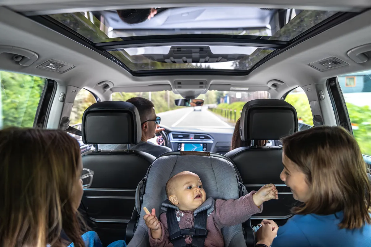 Family road trip with panoramic roof. Baby in car seat reaching sister