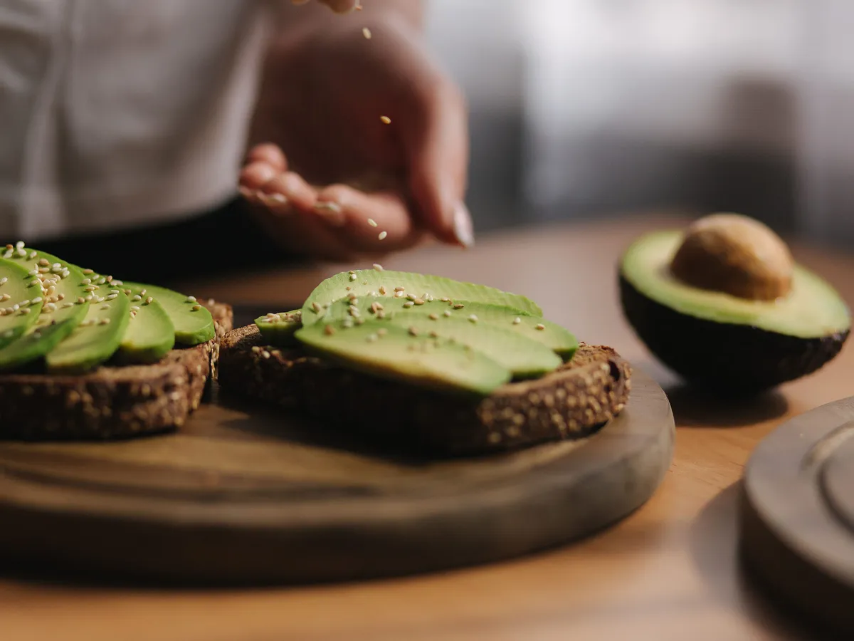 Woman making vegan sandwich using rye bread avocado and sesame seeds.