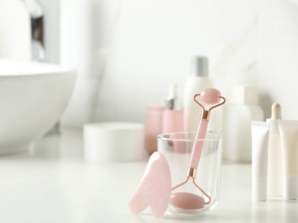 Natural face roller and gua sha tool on counter in bathroom. Space for text