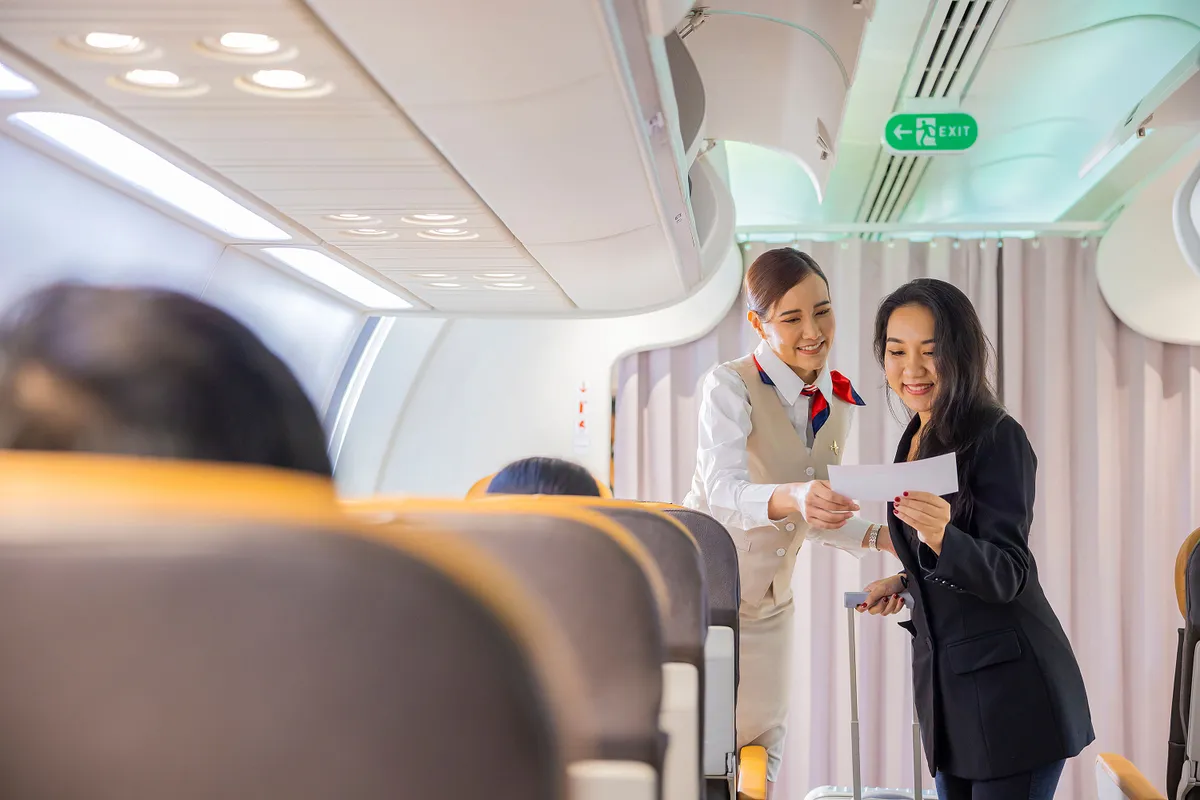 Beautiful Asian female flight attendants in uniform standing at the airplane entrance service take care of asian woman passengers checking seats boarding pass on the airplane before flight traveling.